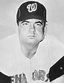 An man in a light baseball jersey and dark cap