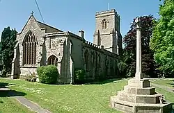 Stone church with arched window and square tower, with a stepped churchyard cross to the right
