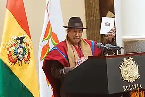 Rafael Quispe, dressed in indigenous garb, holds up a copy of the Bolivian Constitution.