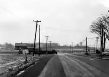Black and white image of a two lane road travelling through muddy fields