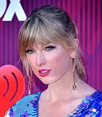 A color headshot of singer Taylor Swift posing for a photograph in front of a step and repeat.