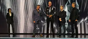 On stage, Timothée Chalamet stands to the left while four game developers accept an award at right, one dressed in armor.