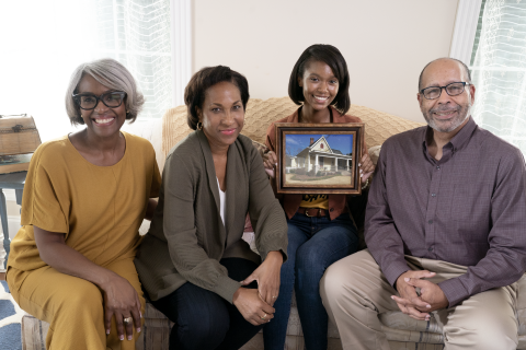 an african american family sits on a couch holding a picture of a home.